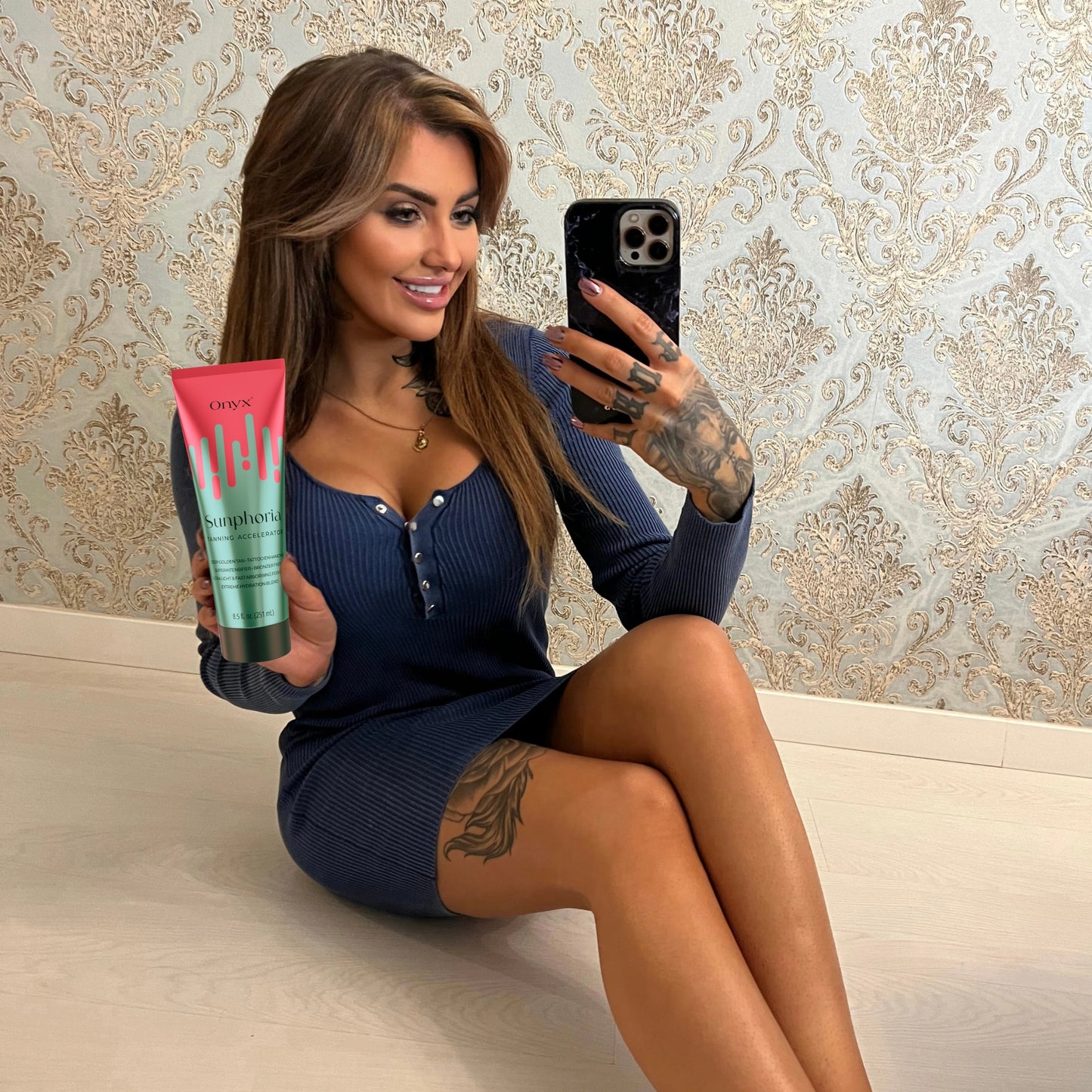 Frau mit Tattoos hält Onyx Sunphoria Bräunungslotion beim Spiegelselfie