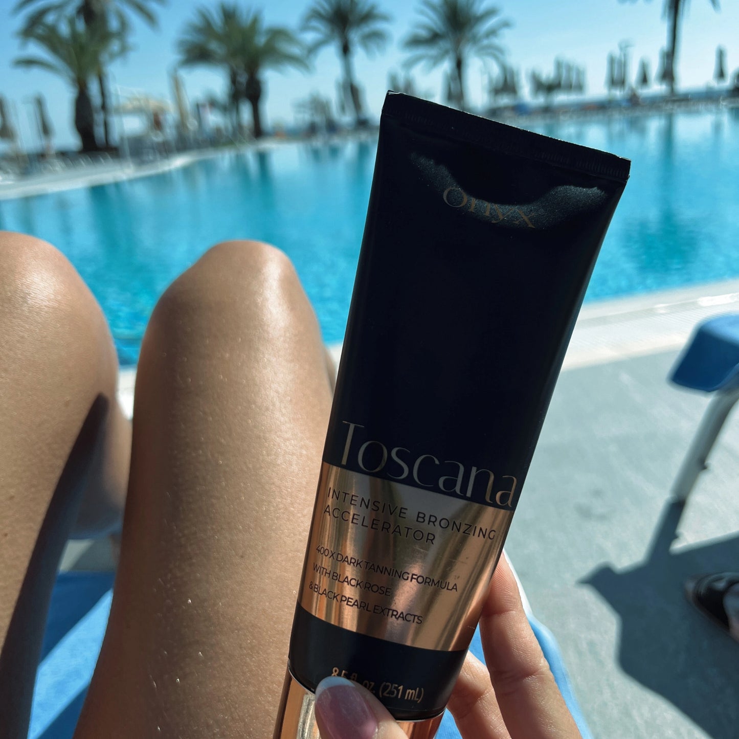 Onyx Toscana Bräunungslotion wird vor gebräunten Beinen am Pool gehalten