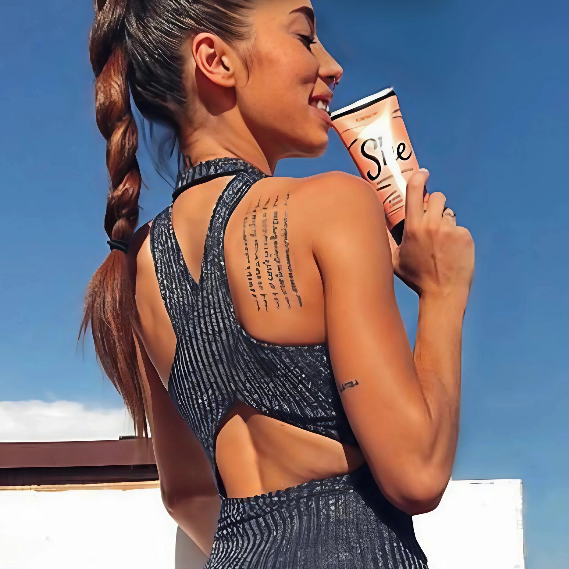 Sportliche Frau zeigt ihr Tattoo am Rücken und hält die Onyx She Bräunungslotion, perfekte Kombination aus Fitness und femininer Hautpflege beim Bräunen