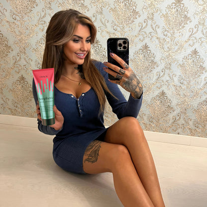 Frau mit Tattoos hält Onyx Sunphoria Bräunungslotion beim Spiegelselfie