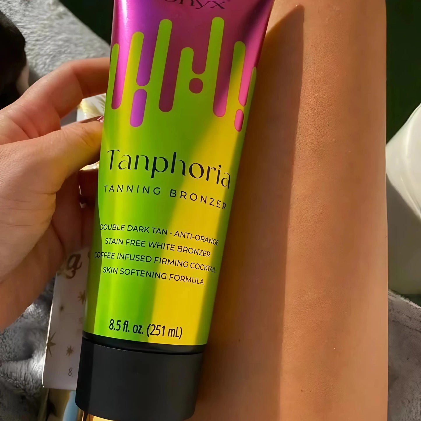 Lächelnde Frau in weißem Kleid zeigt Tanphoria Tanning Bronzer