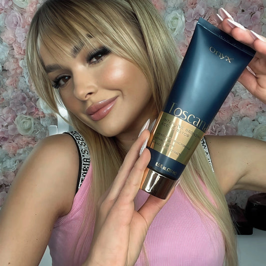 Blonde Frau mit rosa Top lächelt und präsentiert Onyx Toscana Lotion vor Blumenhintergrund