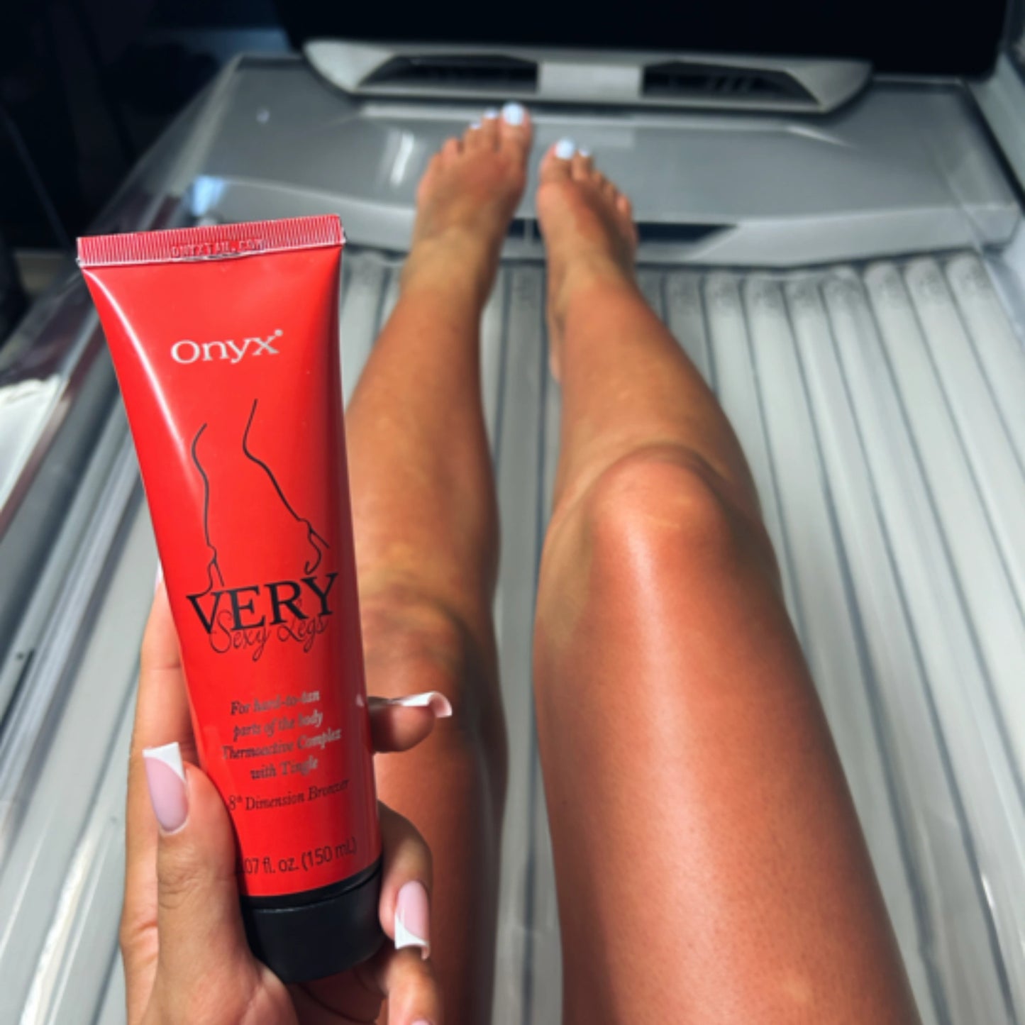 Getönte Beine einer Frau nach der Anwendung von Onyx Very Sexy Legs im Solarium, Lotion in der Hand gehalten